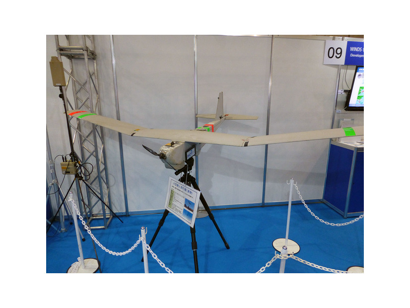 「ワイヤレスジャパン2015」のNICTブースに展示されていた小型無人飛行機は翼長約2.8m，重量約6Kg、連続飛行時間は2～3時間程度。2GHz帯を使用し通信可能区域は約15Kmとなっている（撮影：編集部）