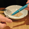 写真：ペン軸のカラリングについて語る岩井氏と同氏愛用の万年筆、ときにこのペン先から生み出される言葉が顧客の安全を支える